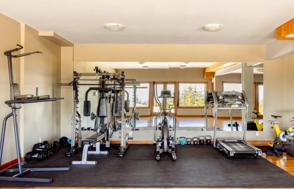 Fitness room at Halo Ridge Recovery with a treadmill, elliptical, weight station, kettlebells, and a mirrored wall