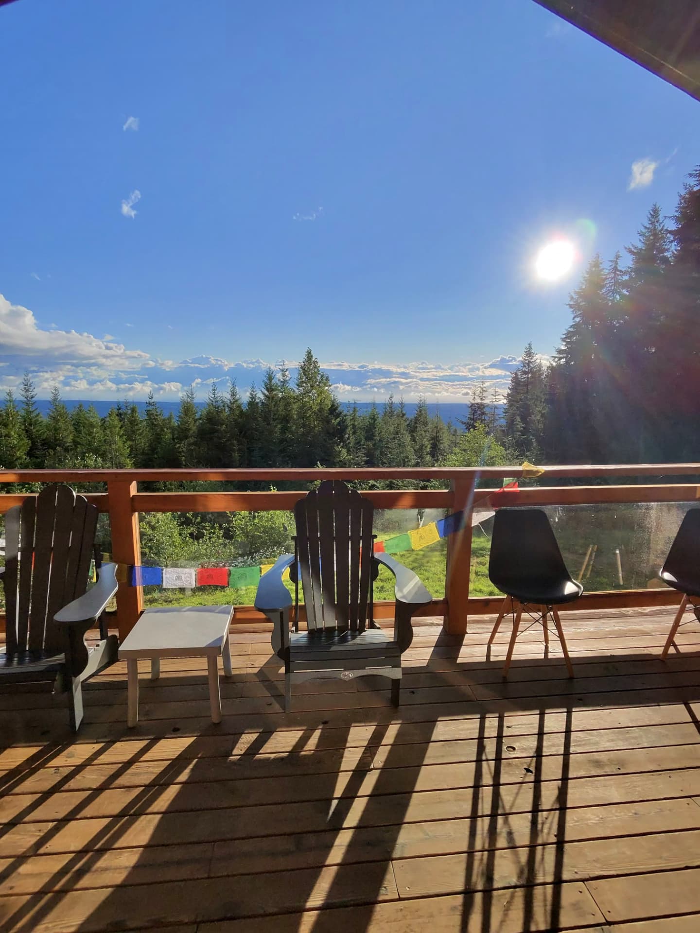 Wooden deck at Halo Ridge Recovery with Adirondack chairs and prayer flags looking out over treetops to the ocean and open sky