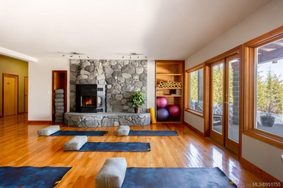 Yoga room at Halo Ridge Recovery with mats and bolsters laid out in front of a river-rock fireplace and windows onto the forest