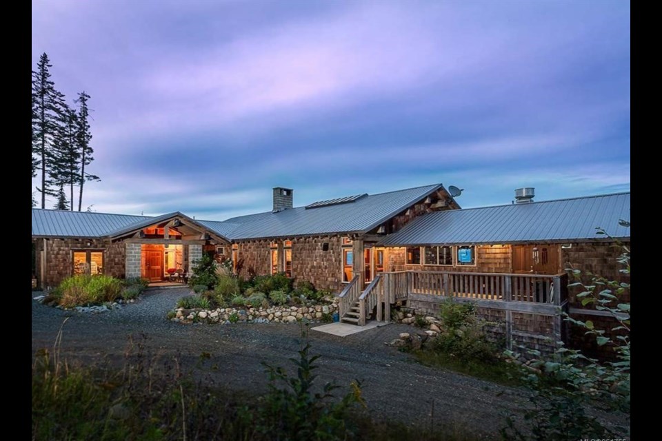 Shingled timber lodge at Halo Ridge Recovery at dusk, warm light in the entryway and a gravel drive curving past native planting